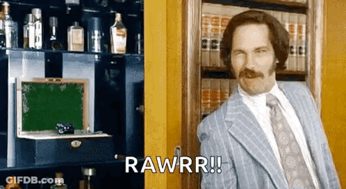 A Man In A Suit And Tie Is Standing In Front Of A Bookshelf And Saying Rawrr ! GIF