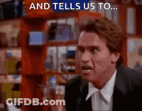 A Man In A Suit And Tie Is Standing In Front Of A Bookshelf And Talking To Someone . GIF