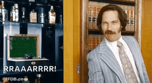 A Man In A Suit And Tie Is Standing In Front Of A Bookshelf With Bottles Of Alcohol . GIF