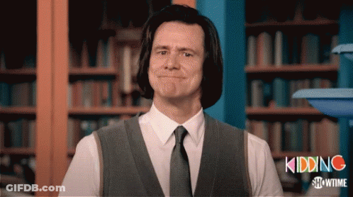A Man In A Suit And Tie Is Standing In Front Of A Bookshelf With The Words Kidding Showtime On The Bottom GIF