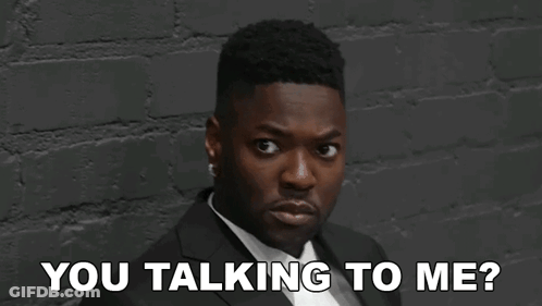 A Man In A Suit And Tie Is Standing In Front Of A Brick Wall And Saying `` You Talking To Me ? '' GIF