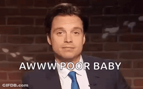 A Man In A Suit And Tie Is Standing In Front Of A Brick Wall And Talking Into A Microphone . GIF
