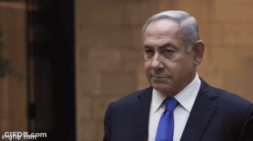 A Man In A Suit And Tie Is Standing In Front Of A Brick Wall GIF