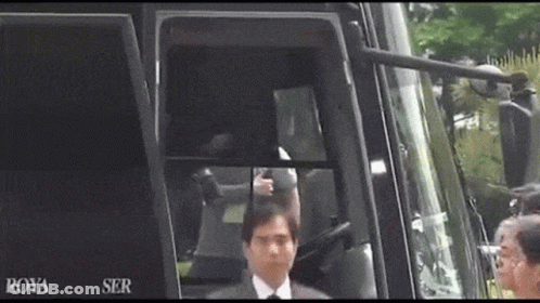 A Man In A Suit And Tie Is Standing In Front Of A Bus That Says Roya Ser On It GIF