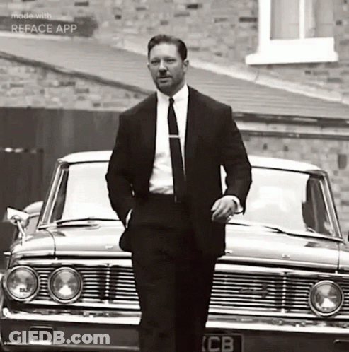 A Man In A Suit And Tie Is Standing In Front Of A Car . GIF