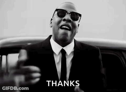 A Man In A Suit And Tie Is Standing In Front Of A Car And Giving A Thanks Sign . GIF
