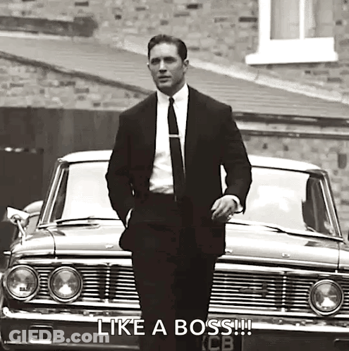 A Man In A Suit And Tie Is Standing In Front Of A Car In A Black And White Photo . GIF