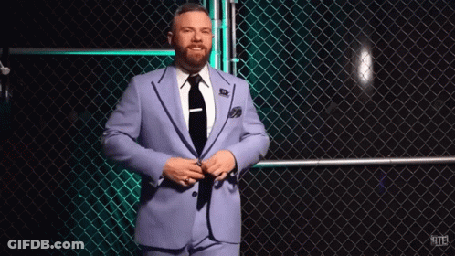 A Man In A Suit And Tie Is Standing In Front Of A Chain Link Fence GIF