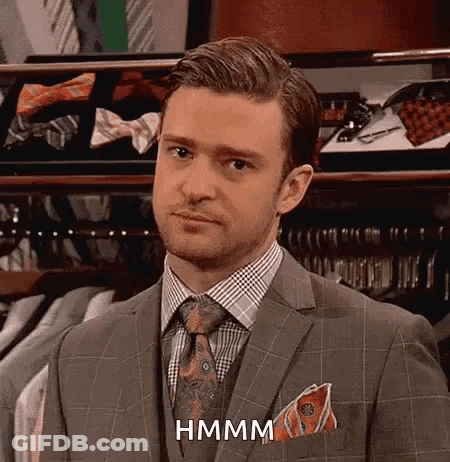 A Man In A Suit And Tie Is Standing In Front Of A Closet Filled With Shirts And Ties . GIF