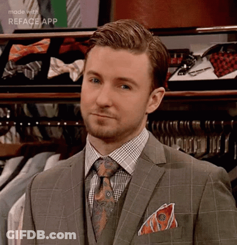 A Man In A Suit And Tie Is Standing In Front Of A Closet Filled With Shirts And Ties . GIF