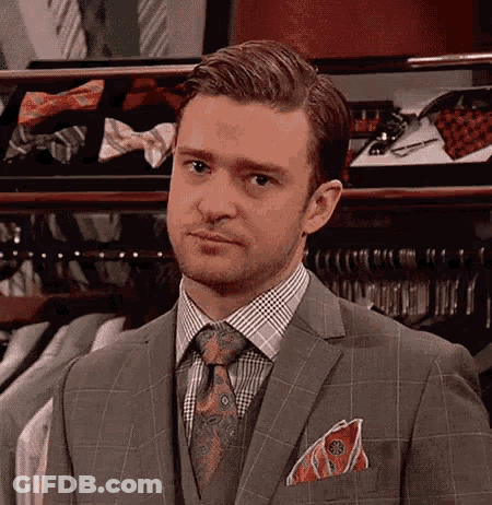A Man In A Suit And Tie Is Standing In Front Of A Closet Filled With Ties . GIF
