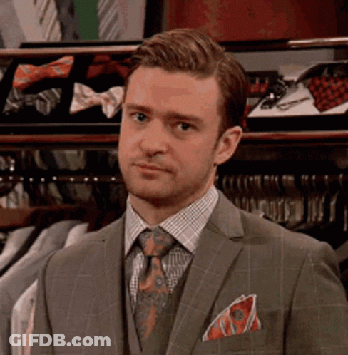 A Man In A Suit And Tie Is Standing In Front Of A Closet Filled With Ties . GIF