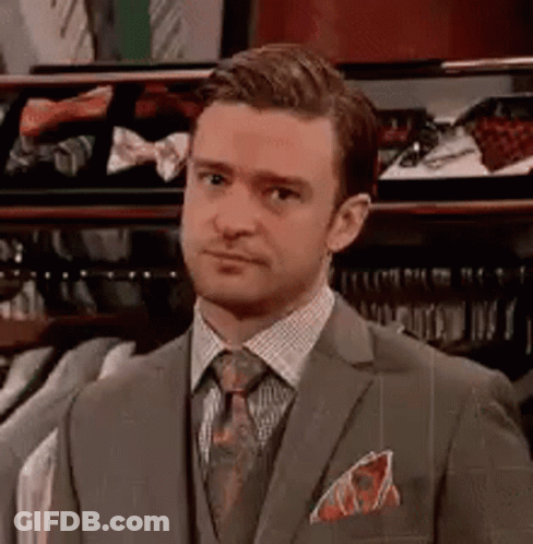 A Man In A Suit And Tie Is Standing In Front Of A Closet Filled With Ties . GIF