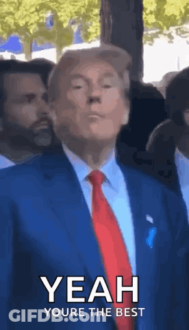A Man In A Suit And Tie Is Standing In Front Of A Crowd And Making A Funny Face . GIF