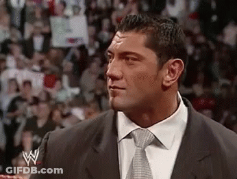 A Man In A Suit And Tie Is Standing In Front Of A Crowd In A Ring . GIF