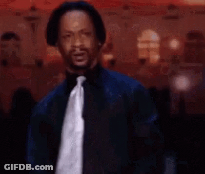 A Man In A Suit And Tie Is Standing In Front Of A Crowd In A Room . GIF