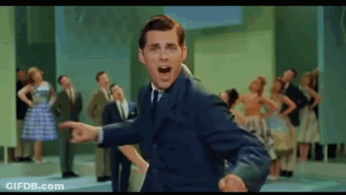 A Man In A Suit And Tie Is Standing In Front Of A Crowd Of People . GIF