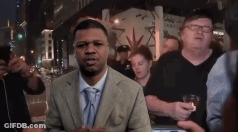 A Man In A Suit And Tie Is Standing In Front Of A Crowd Of People GIF