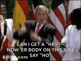 A Man In A Suit And Tie Is Standing In Front Of A Crowd Of People And Flags . GIF