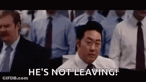 A Man In A Suit And Tie Is Standing In Front Of A Crowd Of People And Says `` He 'S Not Leaving ! '' GIF