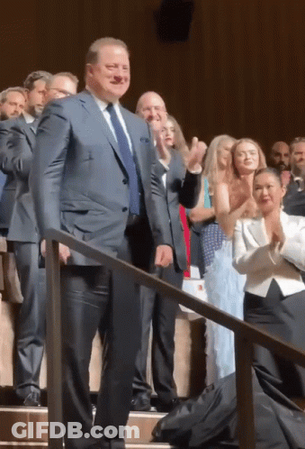 A Man In A Suit And Tie Is Standing In Front Of A Crowd Of People GIF