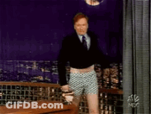 A Man In A Suit And Tie Is Standing In Front Of A Curtain That Says Nbc GIF