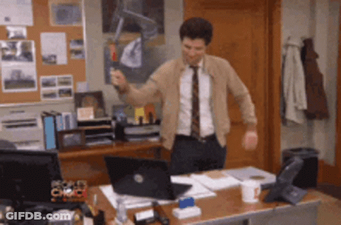A Man In A Suit And Tie Is Standing In Front Of A Desk With A Laptop GIF