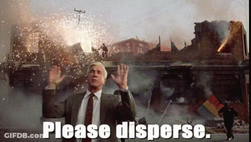 A Man In A Suit And Tie Is Standing In Front Of A Destroyed Building And Says Please Disperse GIF