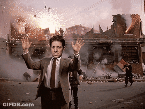 A Man In A Suit And Tie Is Standing In Front Of A Destroyed Building GIF