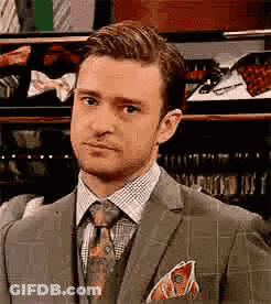A Man In A Suit And Tie Is Standing In Front Of A Display Of Ties . GIF