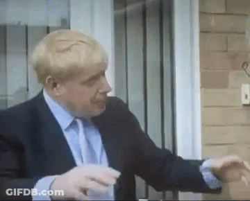 A Man In A Suit And Tie Is Standing In Front Of A Door And Talking On A Cell Phone . GIF