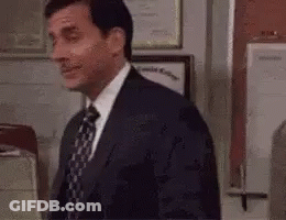 A Man In A Suit And Tie Is Standing In Front Of A Door In An Office . GIF