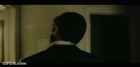 A Man In A Suit And Tie Is Standing In Front Of A Door . GIF