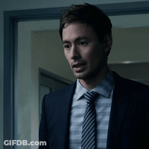 A Man In A Suit And Tie Is Standing In Front Of A Door GIF