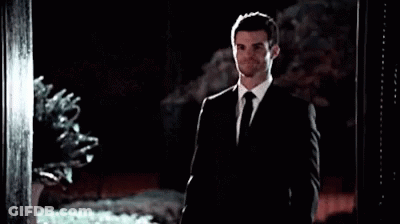 A Man In A Suit And Tie Is Standing In Front Of A Doorway . GIF