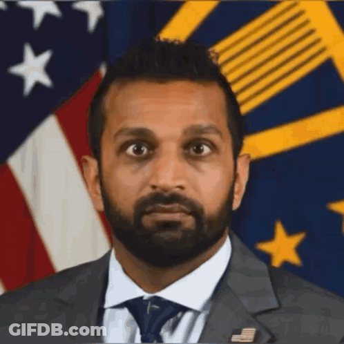 A Man In A Suit And Tie Is Standing In Front Of A Flag GIF