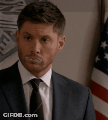 A Man In A Suit And Tie Is Standing In Front Of A Flag GIF