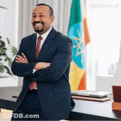 A Man In A Suit And Tie Is Standing In Front Of A Flag With His Arms Crossed And Smiling . GIF