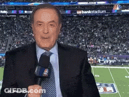 A Man In A Suit And Tie Is Standing In Front Of A Football Field GIF
