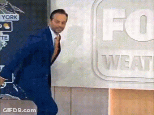 A Man In A Suit And Tie Is Standing In Front Of A Fox Weather Sign . GIF