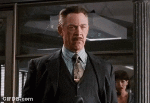 A Man In A Suit And Tie Is Standing In Front Of A Glass Door GIF