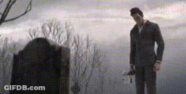 A Man In A Suit And Tie Is Standing In Front Of A Grave In A Cemetery . GIF