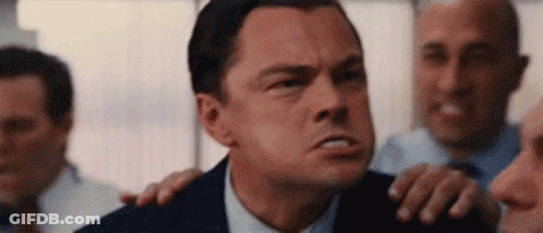 A Man In A Suit And Tie Is Standing In Front Of A Group Of Men And Making A Funny Face . GIF