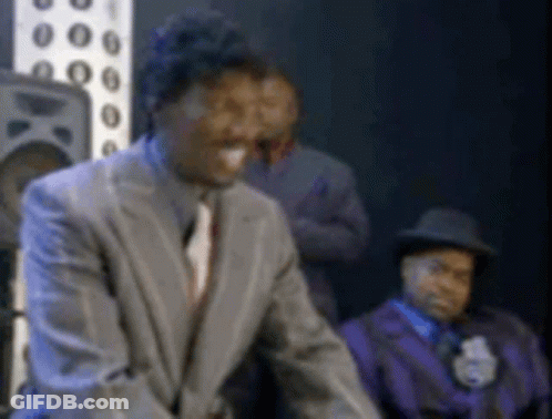 A Man In A Suit And Tie Is Standing In Front Of A Group Of Men . GIF