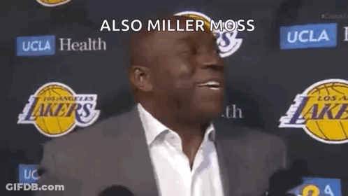 A Man In A Suit And Tie Is Standing In Front Of A Lakers Logo And Talking To The Media . GIF