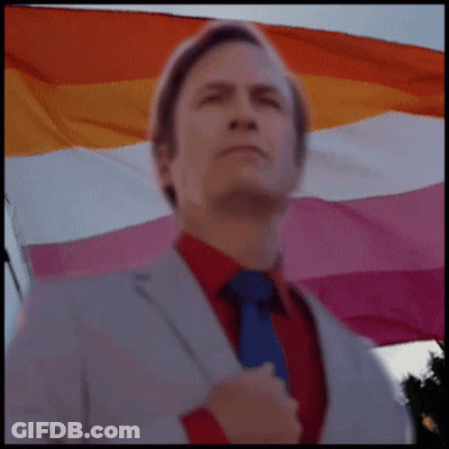 A Man In A Suit And Tie Is Standing In Front Of A Lesbian Flag GIF