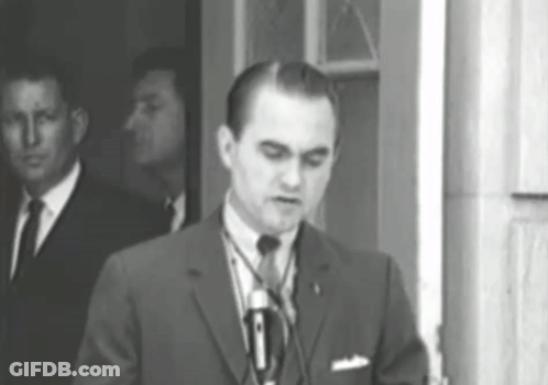 A Man In A Suit And Tie Is Standing In Front Of A Microphone GIF