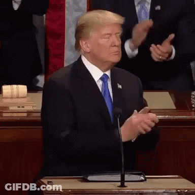 A Man In A Suit And Tie Is Standing In Front Of A Microphone And Clapping His Hands . GIF