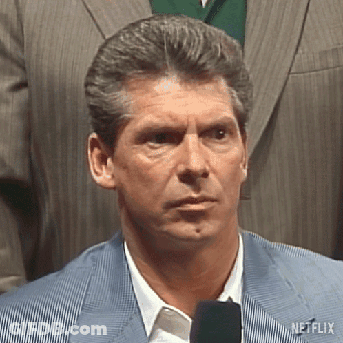 A Man In A Suit And Tie Is Standing In Front Of A Microphone And Looking At The Camera . GIF