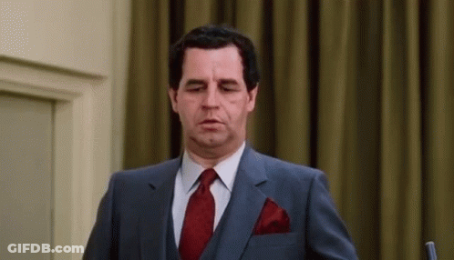 A Man In A Suit And Tie Is Standing In Front Of A Microphone And Making A Funny Face . GIF